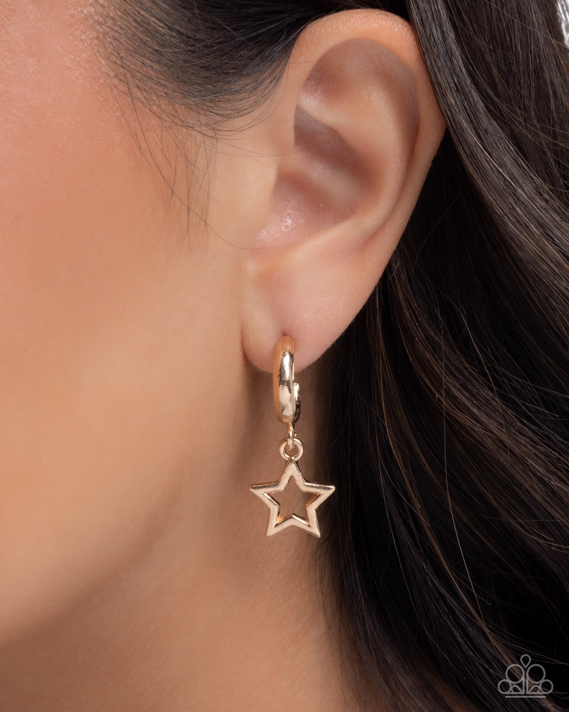 Gold star-shaped earring worn by a person with dark hair.