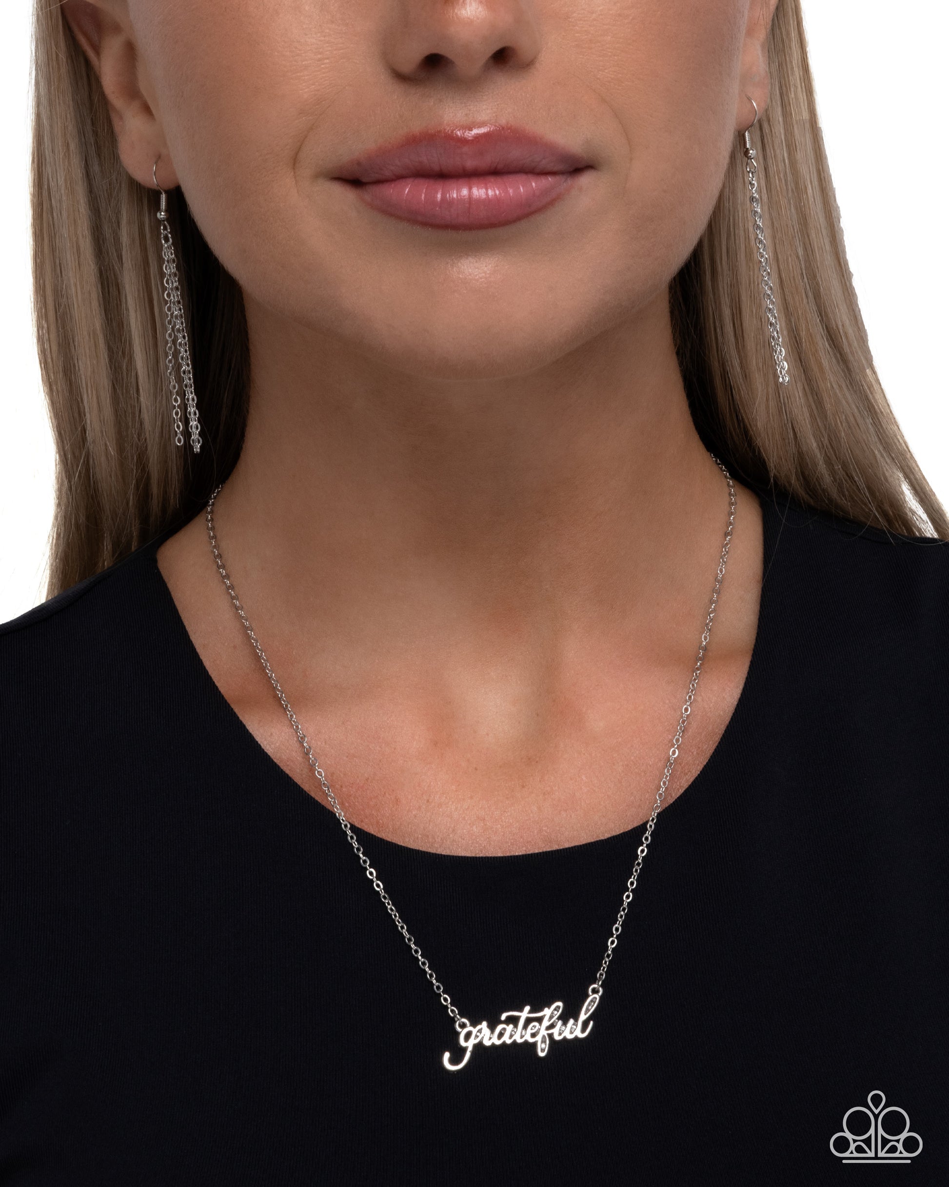 Woman wearing a silver 'grateful' necklace and earrings on a white background