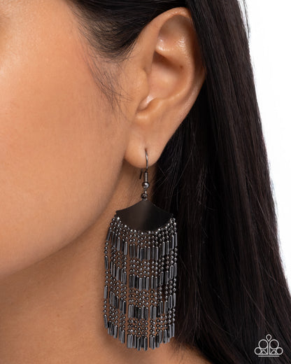 Black fringe earring worn by a person with dark hair on a white background