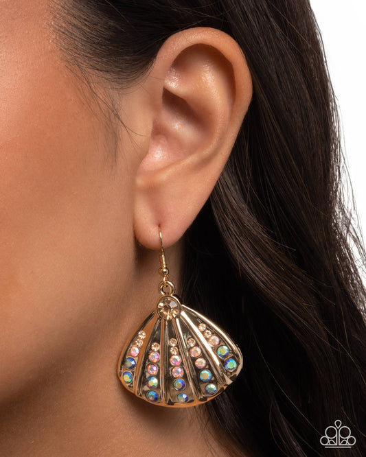 Close-up of an ear wearing a gold shell-shaped earring with colorful stones.