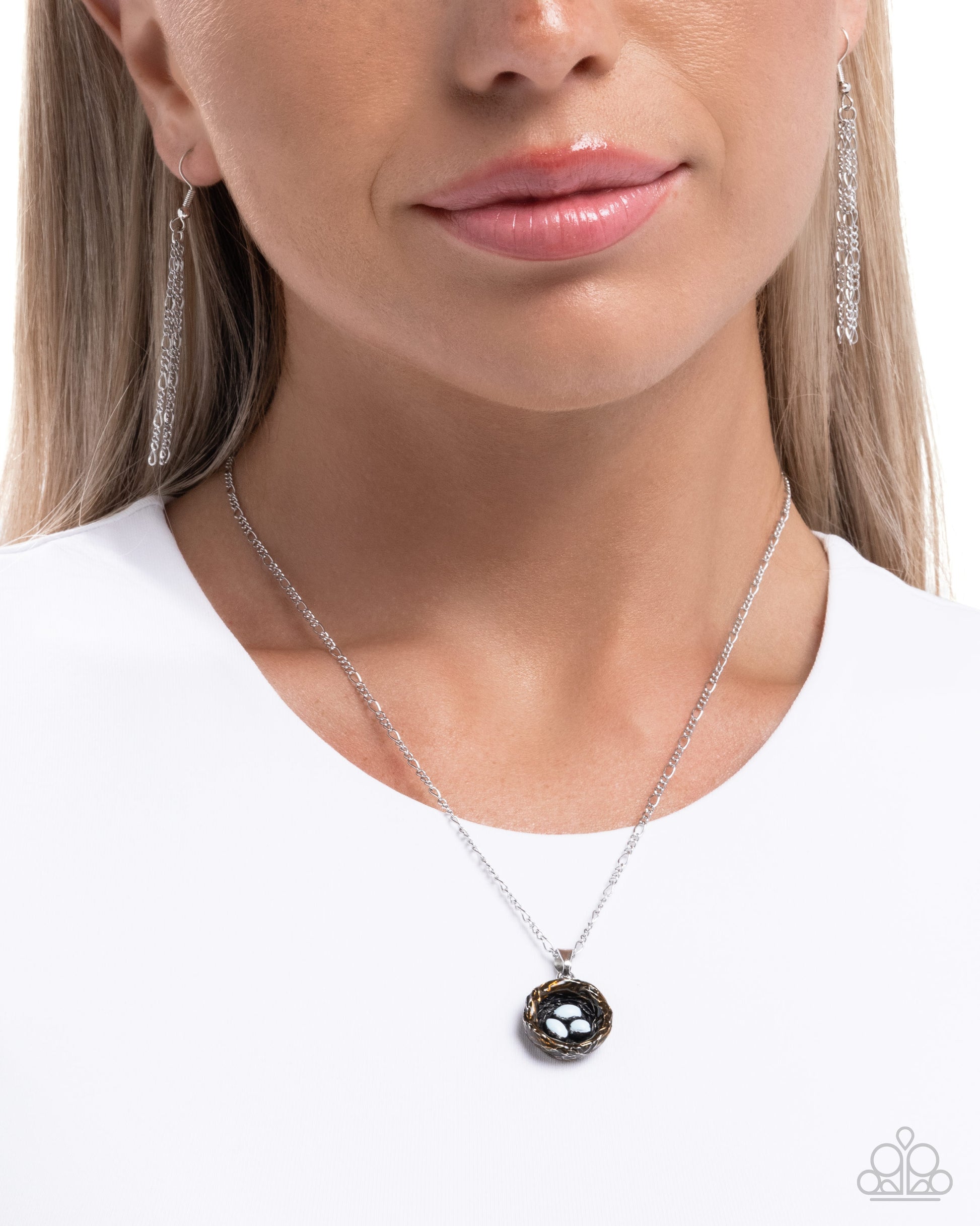 Woman wearing a silver necklace with a black pendant on a white background