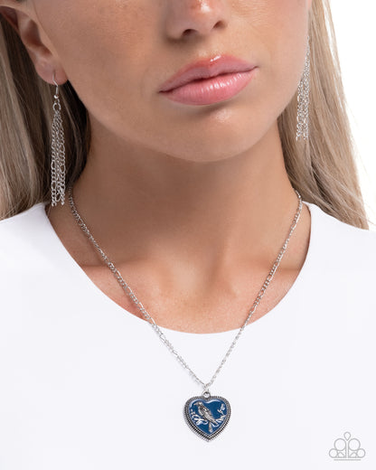 Close-up of a woman wearing a silver necklace with a blue heart pendant on a white background