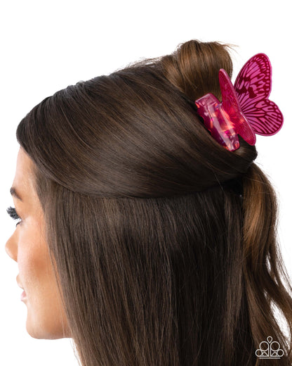 A side profile of a woman with dark brown hair wearing a translucent pink butterfly-shaped hair clip, shown against a plain white background.