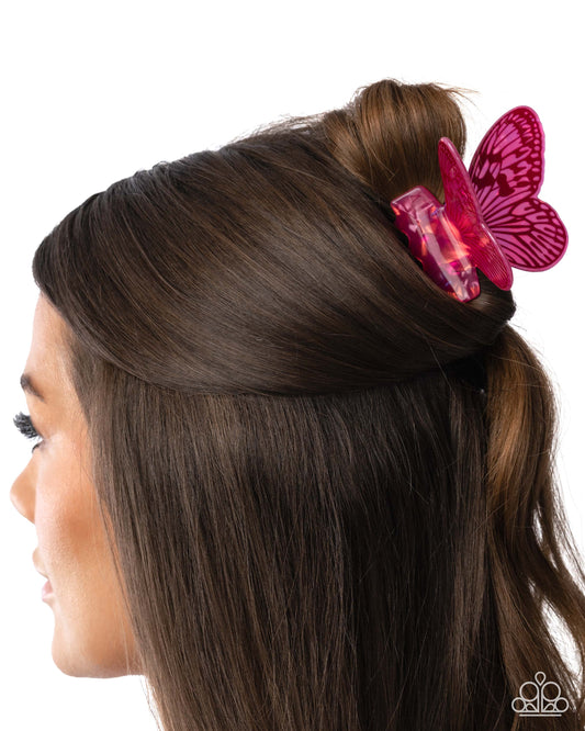 A side profile of a woman with dark brown hair wearing a translucent pink butterfly-shaped hair clip, shown against a plain white background.