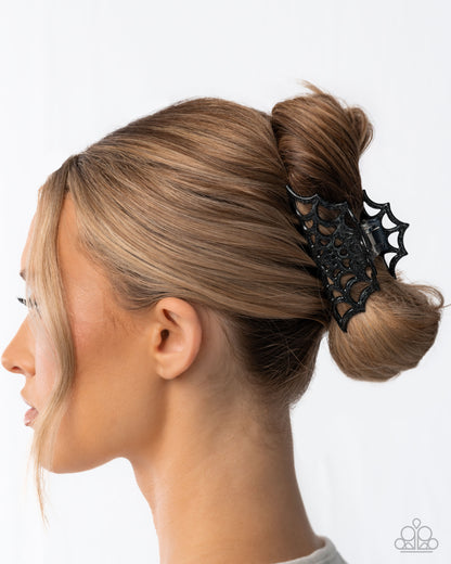 Woman with a bun holding a black spiderweb hair clip against a white background