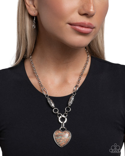 Necklace with a heart-shaped pendant worn by a person on a plain background