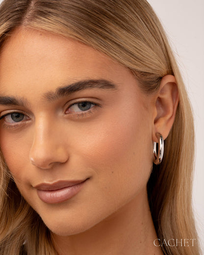 Close-up of a woman wearing silver hoop earrings with a neutral background
