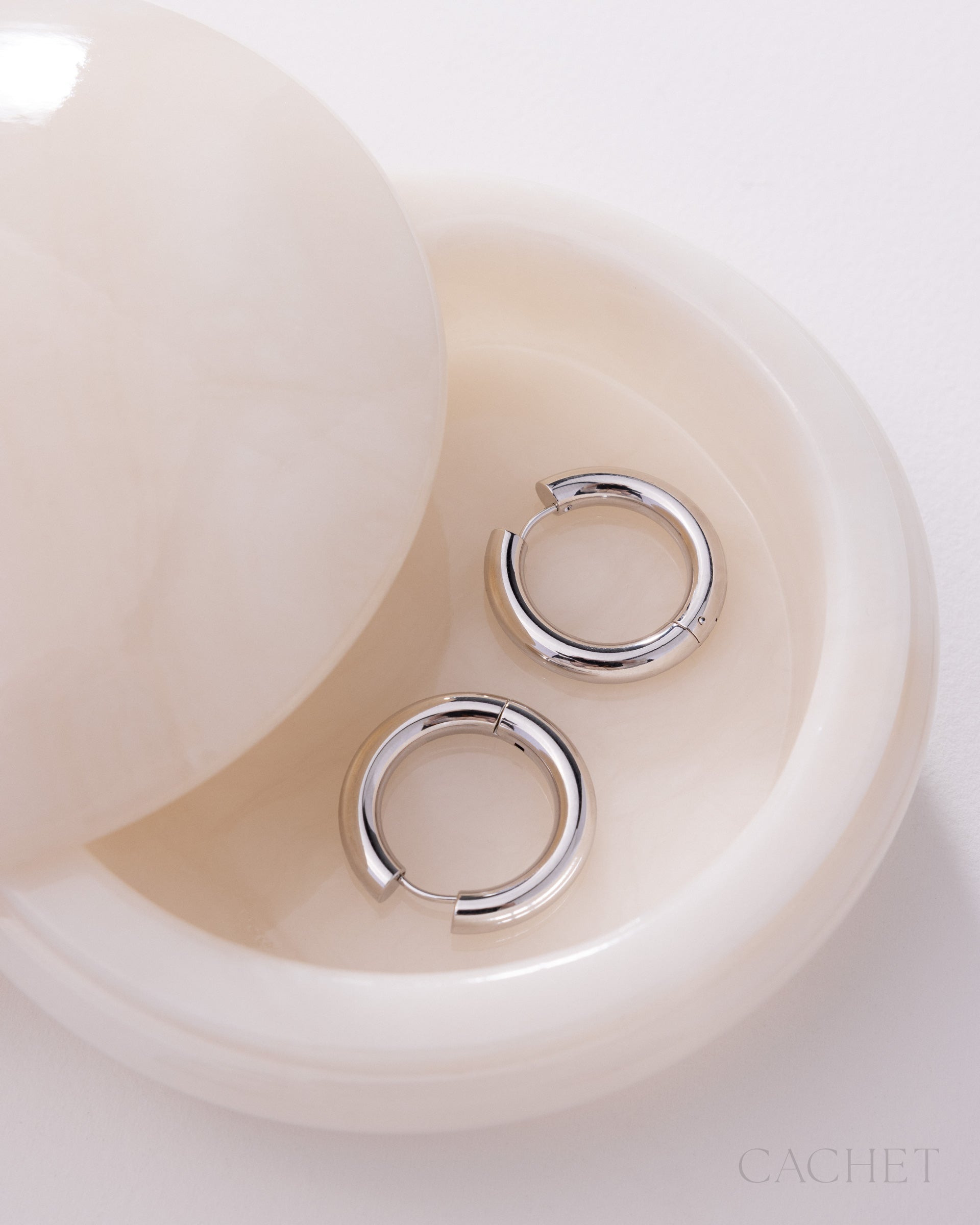Silver hoop earrings on a white shell with 'Cachet' branding.