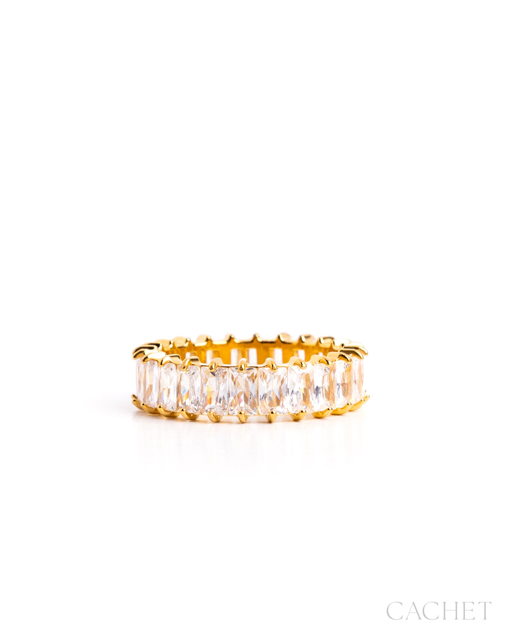 Gold ring with clear gemstones on a white background, featuring the brand 'Cachet'.