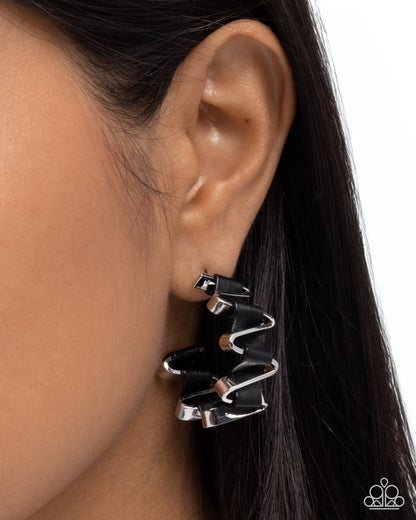 Black and silver earring worn by a person with dark hair.
