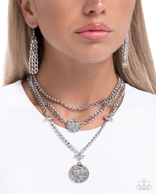 Close-up of a woman wearing multiple silver necklaces and earrings on a white background
