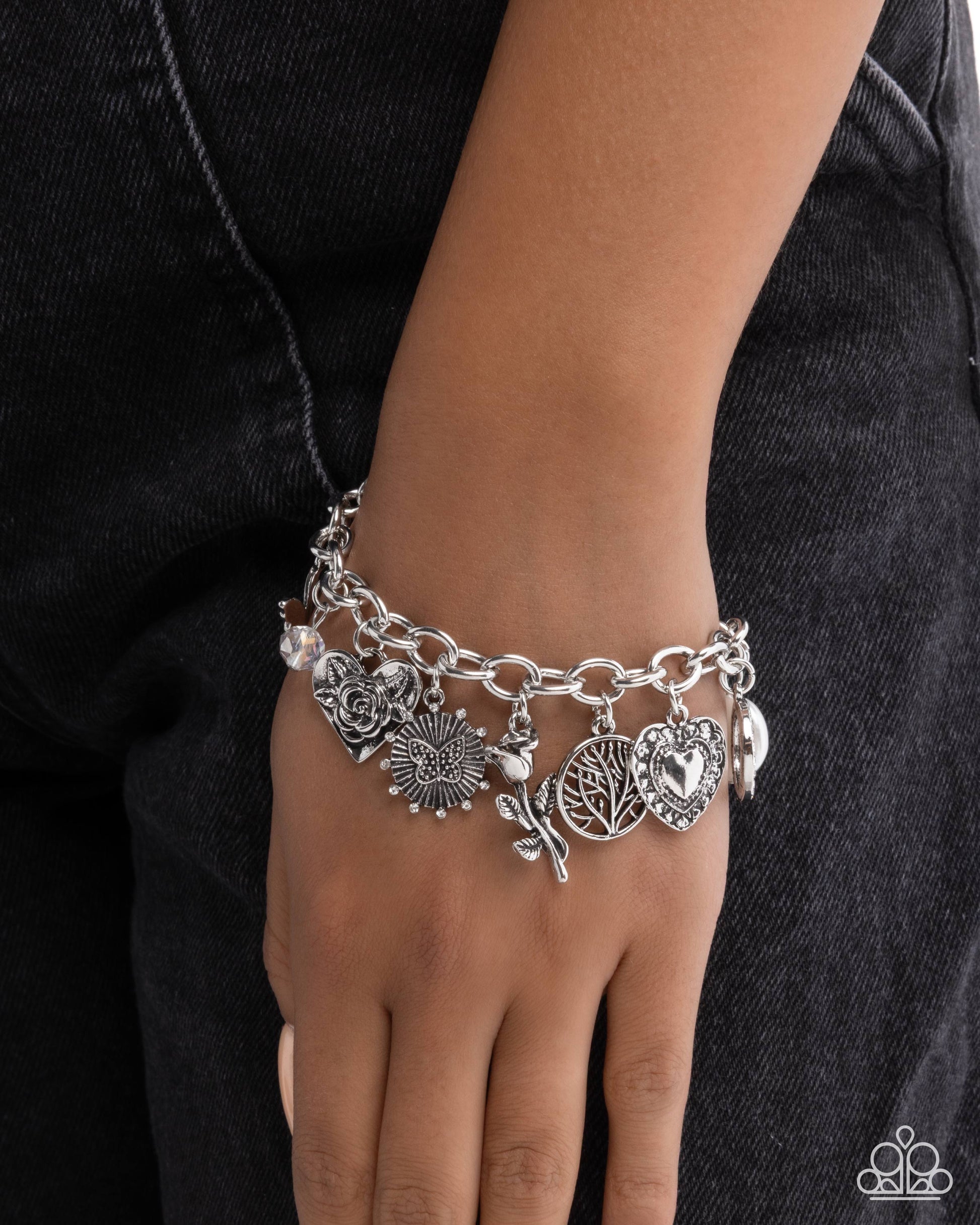Silver charm bracelet on a wrist against a dark background