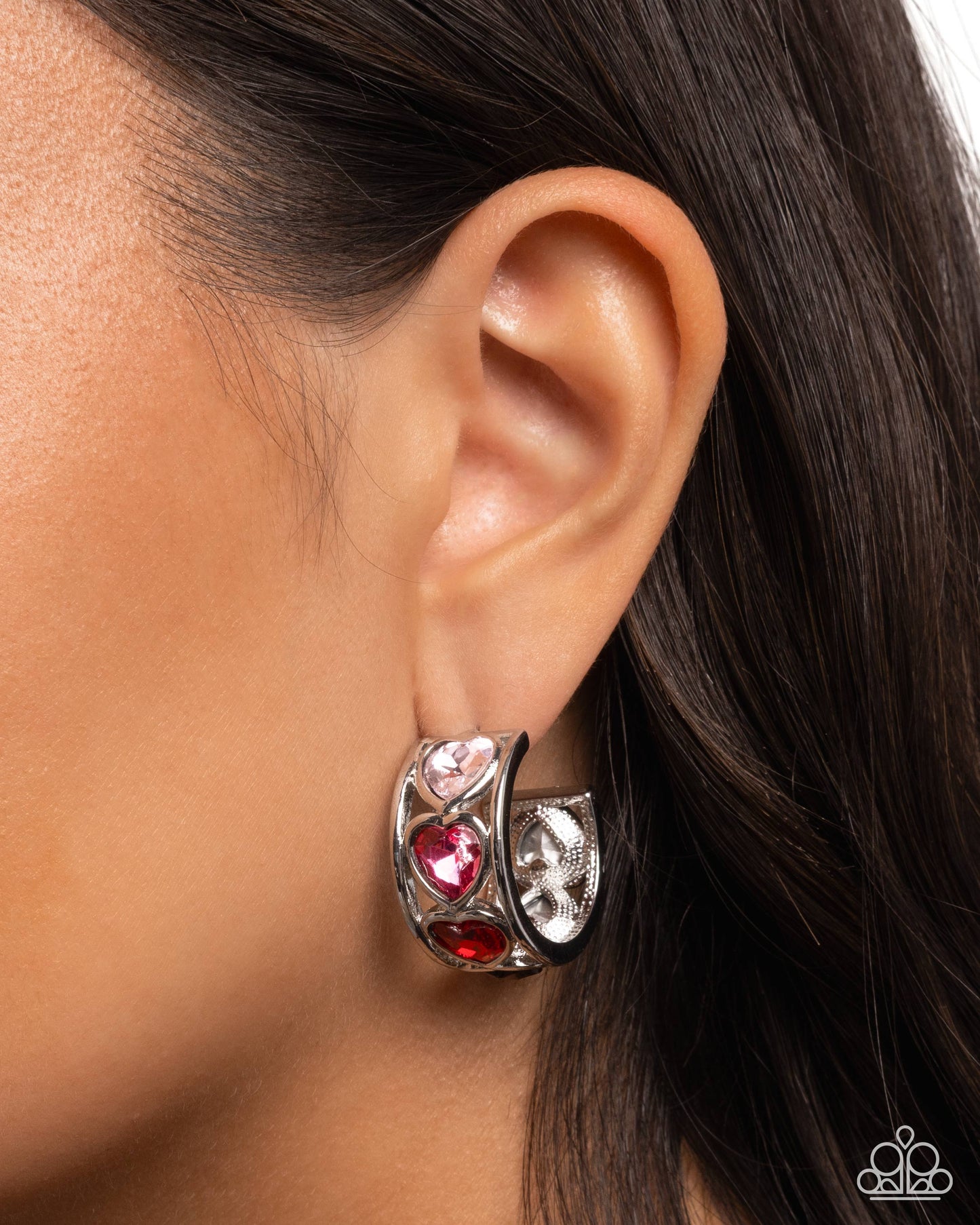 Close-up of an ear wearing a silver hoop earring with red and pink gemstones.