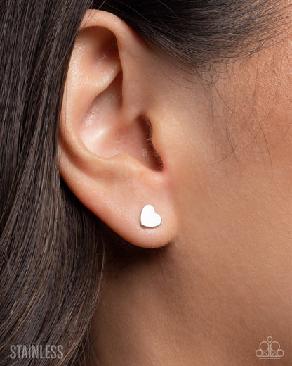 Heart-shaped earring worn on an ear with a blurred background
