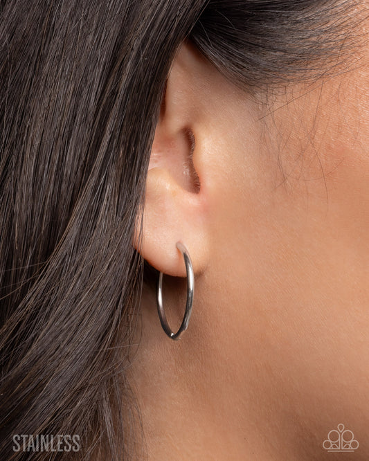 Close-up of an ear wearing a silver hoop earring with hair partially covering the side.