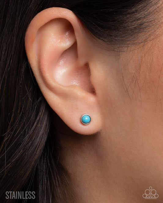 Close-up of an ear wearing a turquoise stud earring with 'Stainless' text below.