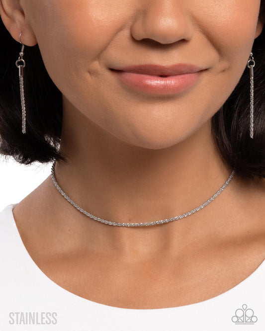 Close-up of a person wearing silver earrings and a choker necklace on a white background.