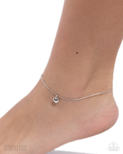 Silver anklet on a foot with a white background