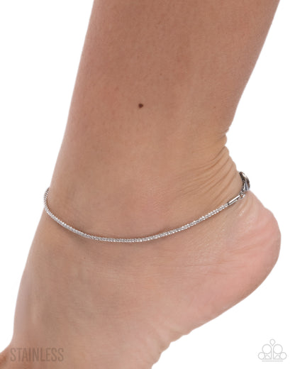 Silver anklet on a person's ankle with a white background