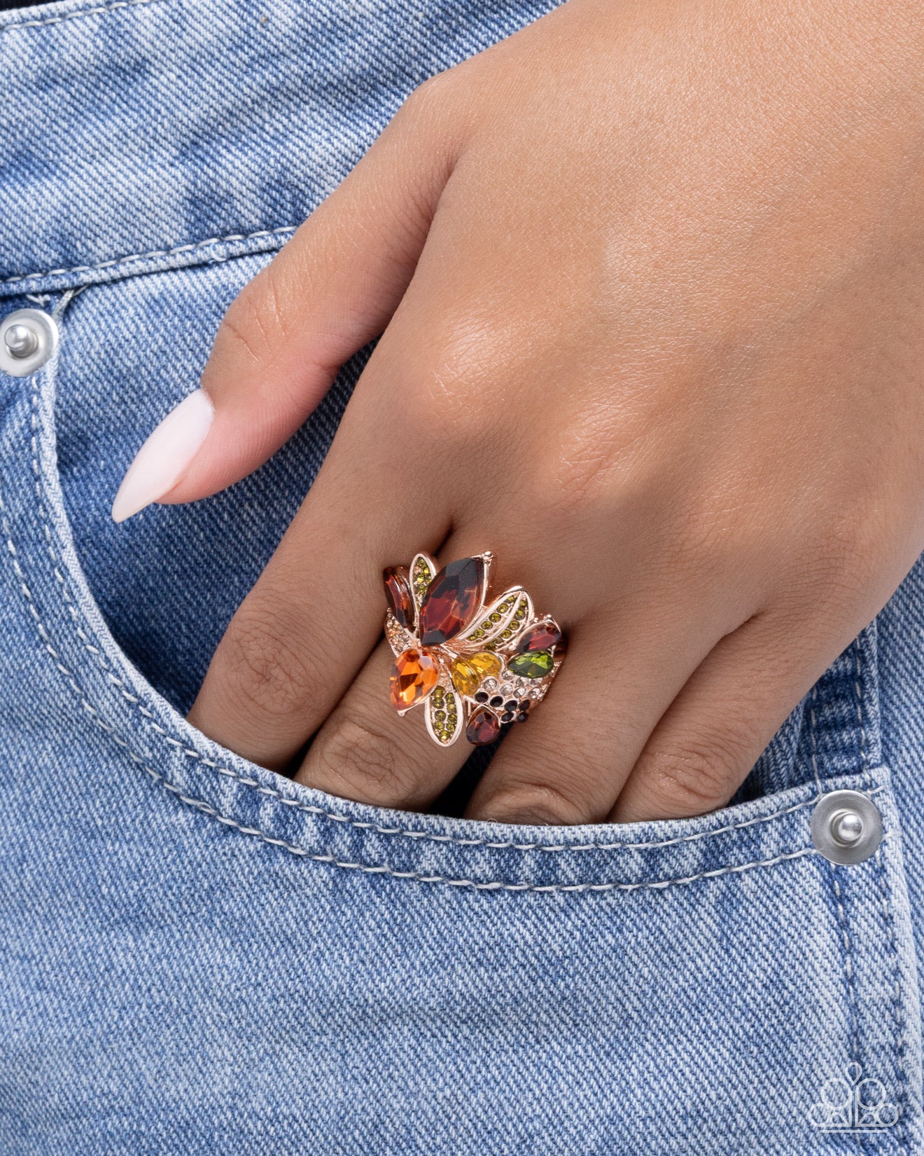 Hand wearing a colorful butterfly ring on denim fabric