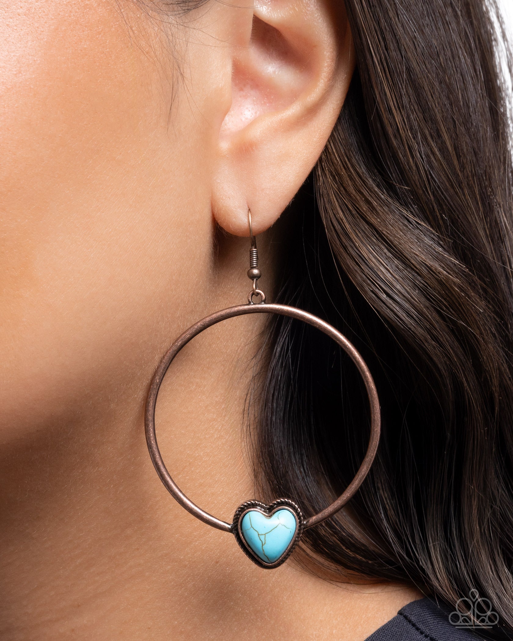 Close-up of an earring with a turquoise heart charm worn by a person.