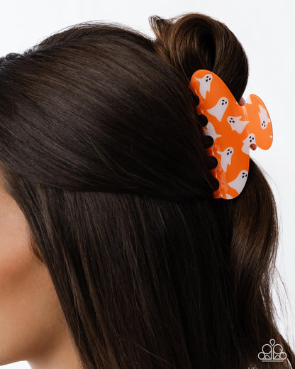 Orange hair clip with ghost design on a person's hair against a white background