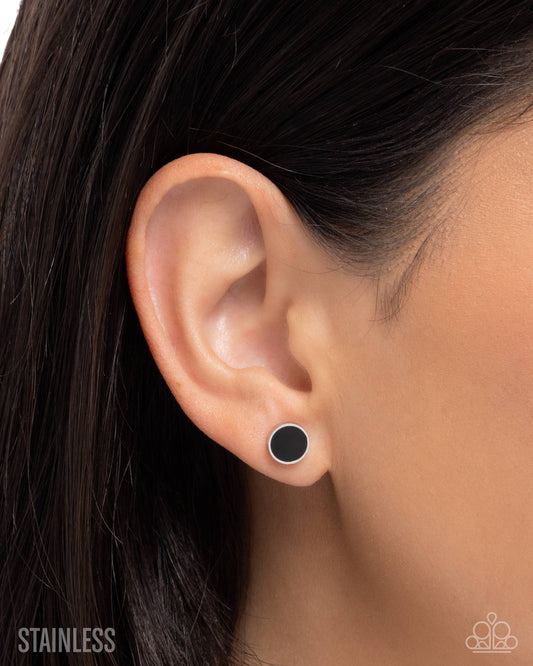 Close-up of an ear wearing a black stud earring with 'Stainless' text.