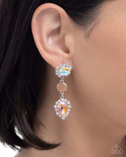 A close-up of a model's ear wearing a double drop earring. The earring features a silver-toned top setting with a small iridescent oval gemstone, a round peach-beige accent stone, and a larger teardrop-shaped iridescent gemstone in a halo setting below.