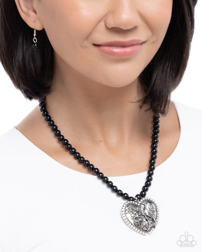 Black beaded necklace with a heart-shaped pendant worn by a model on a white background