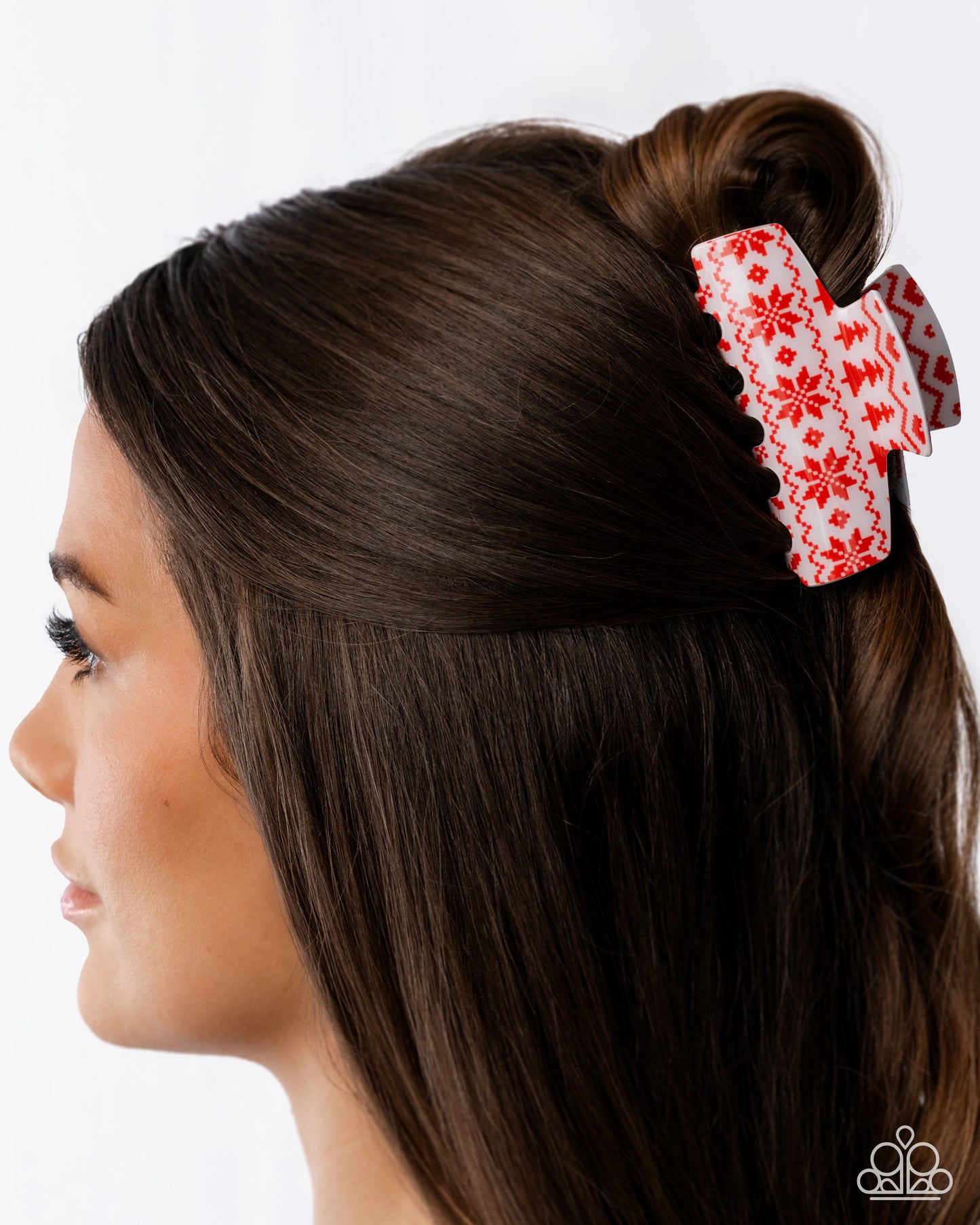 Woman with brown hair styled in a bun with a red and white floral hair clip on a white background