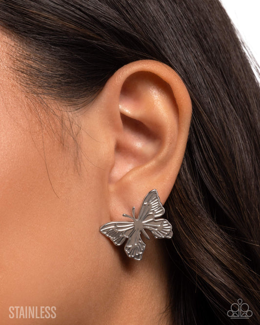 Butterfly earring worn on an ear with a blurred background