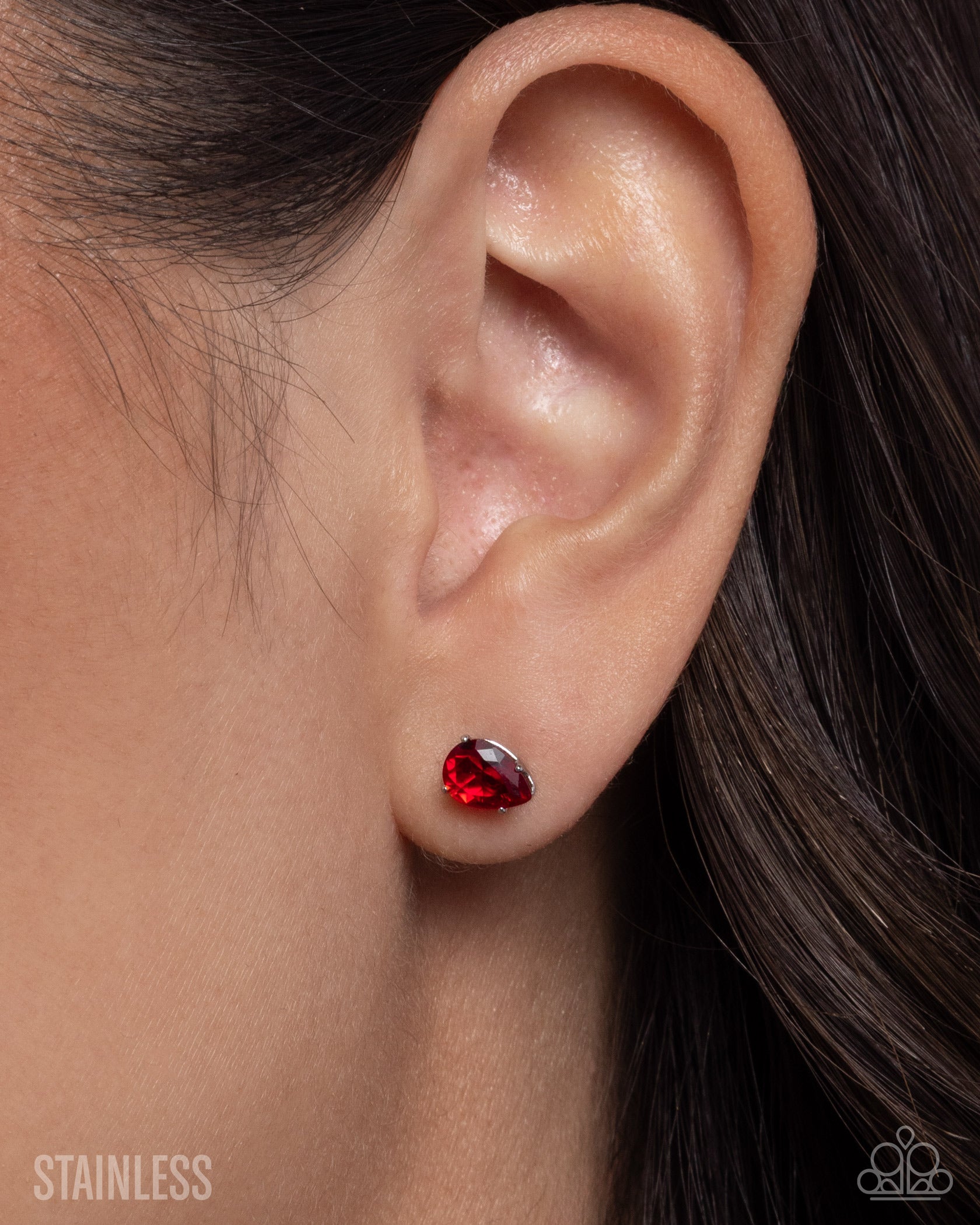 Close-up of an ear wearing a red gemstone earring with blurred hair and skin in the background.
