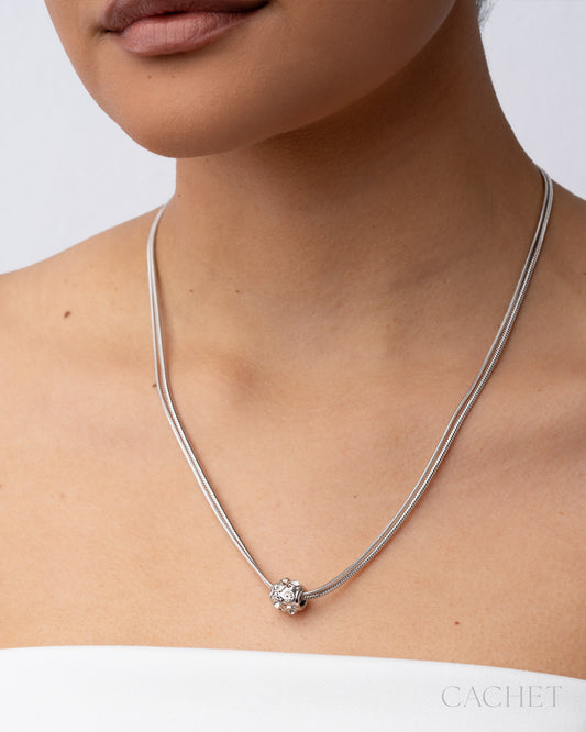 Silver necklace with a pendant on a person against a white background, featuring the brand 'Cachet'.