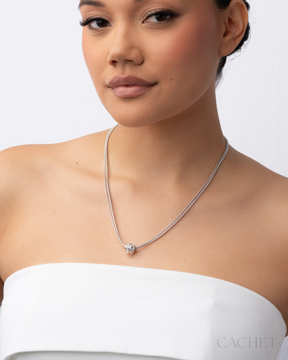 Woman wearing a silver necklace with a visible brand logo on a white background