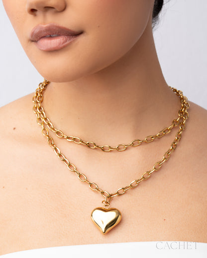 Gold chain necklace with a heart pendant worn by a person on a plain background