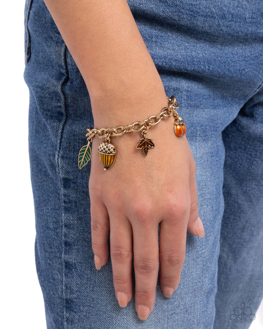 Bracelet with acorn, leaf, and bell charms on a wrist against a blue denim background