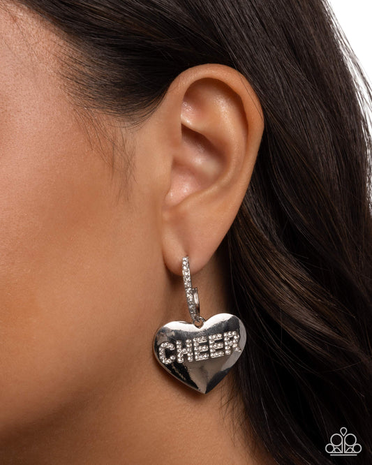 Silver heart-shaped earring with 'CHEER' text worn by a person