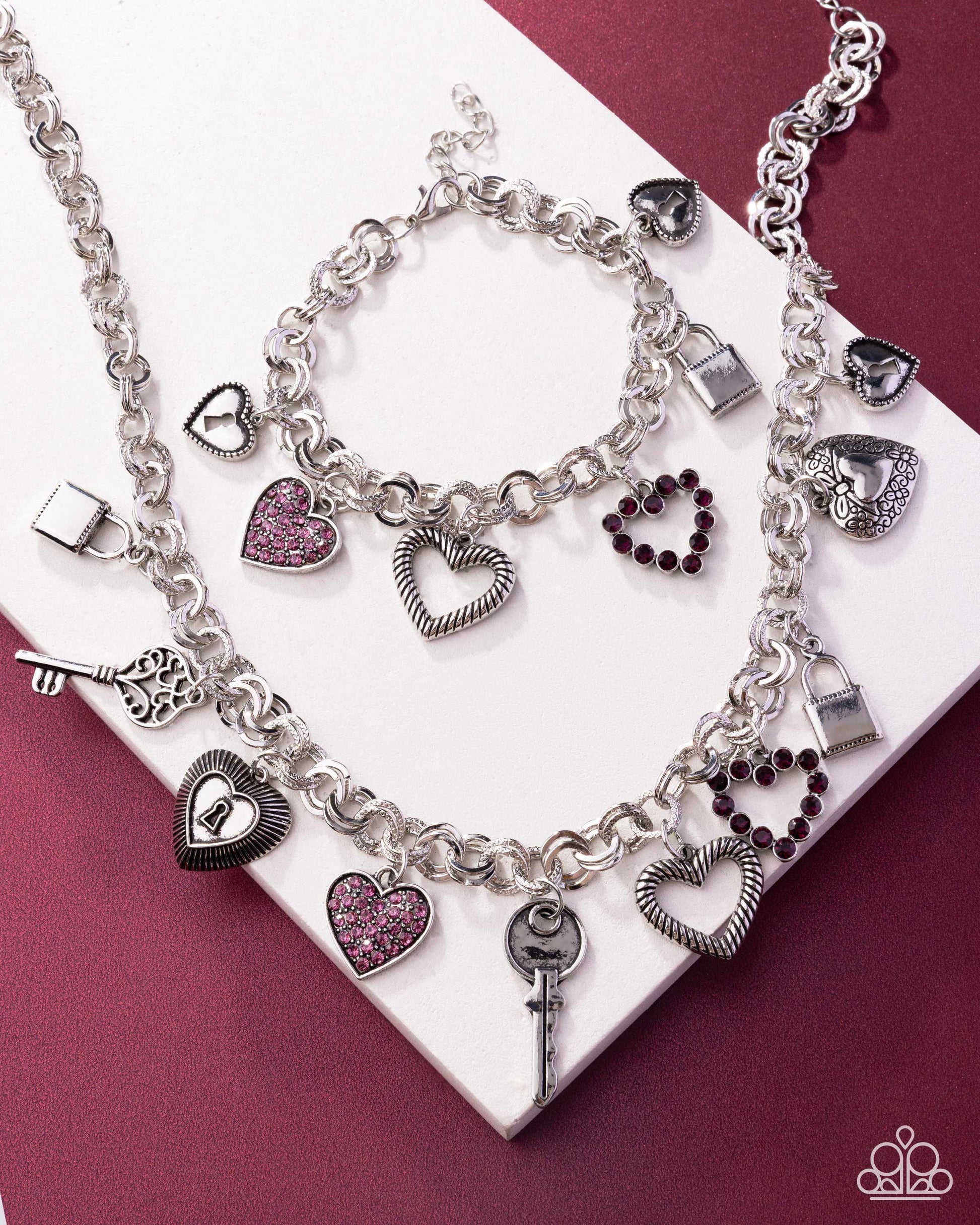 Silver charm bracelet with heart and key charms on a white and maroon background