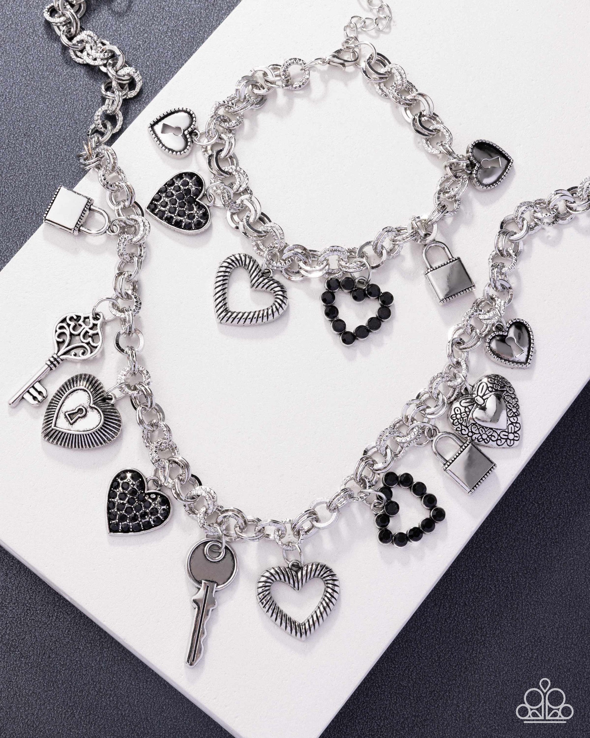 Silver charm bracelet with heart, key, and padlock charms on a white and gray background