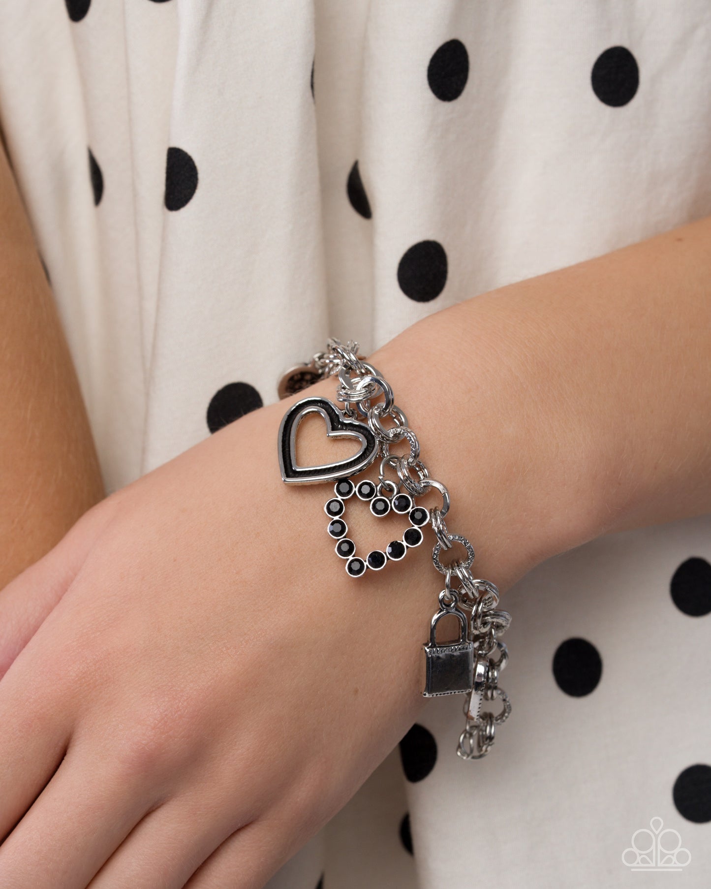 Silver bracelet with heart charm on a wrist against a polka dot background