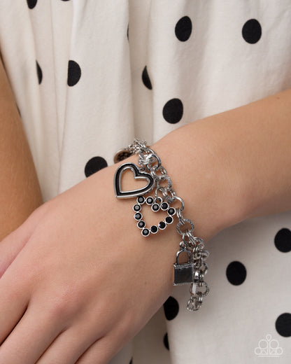 Silver bracelet with heart charm on a wrist against a polka dot background