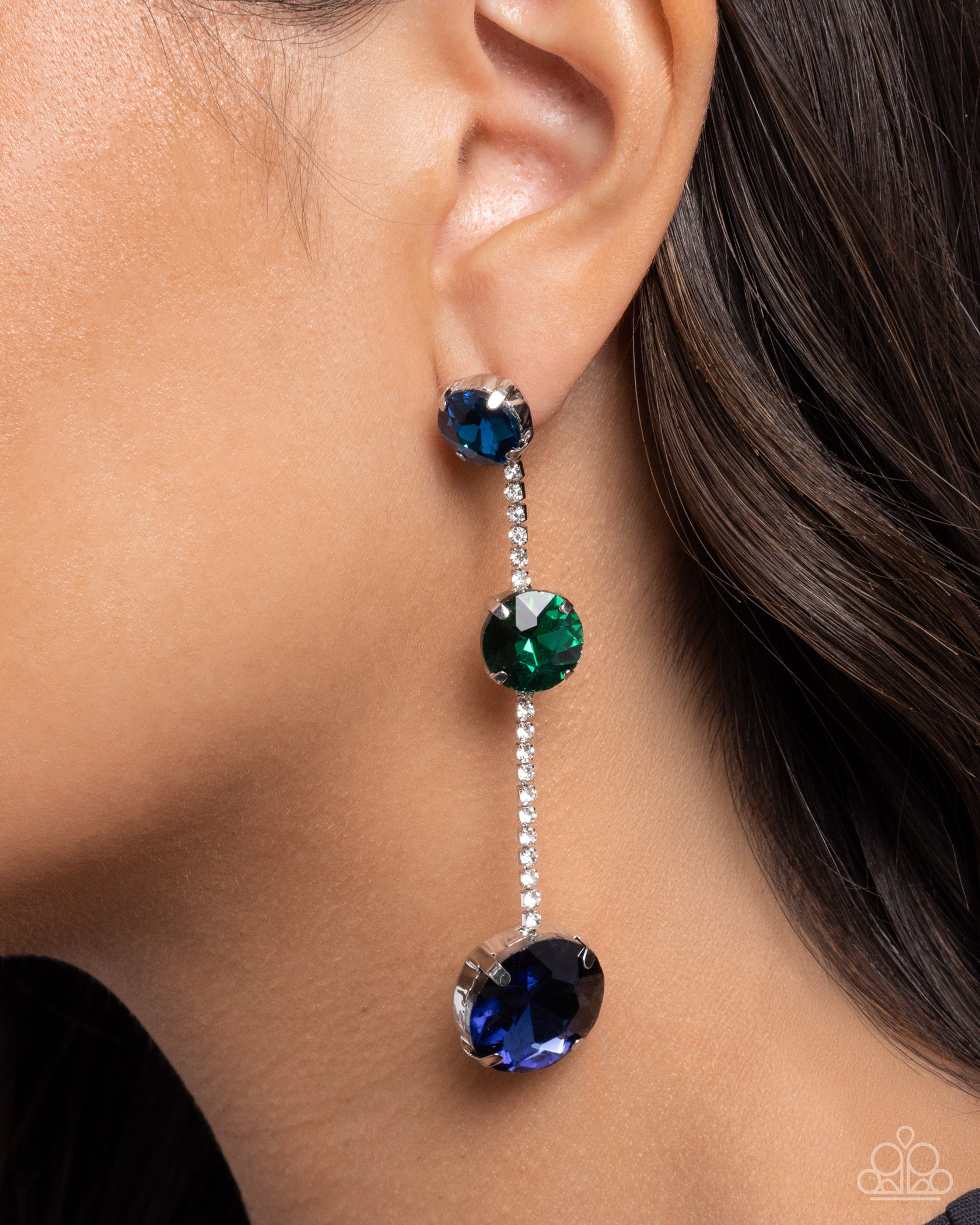 Close-up of an earring with blue and green gemstones on a person's ear.