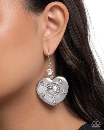 Silver heart-shaped earring with clear gemstones worn by a model