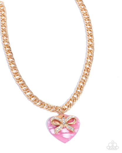 Gold chain necklace with a pink heart pendant and bow on a white background