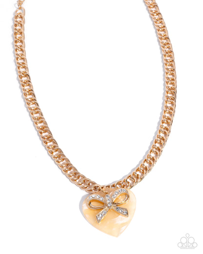 Gold chain necklace with a heart-shaped pendant featuring a bow design on a white background