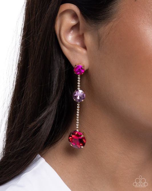 Close-up of an earring with pink and purple gemstones worn by a person.