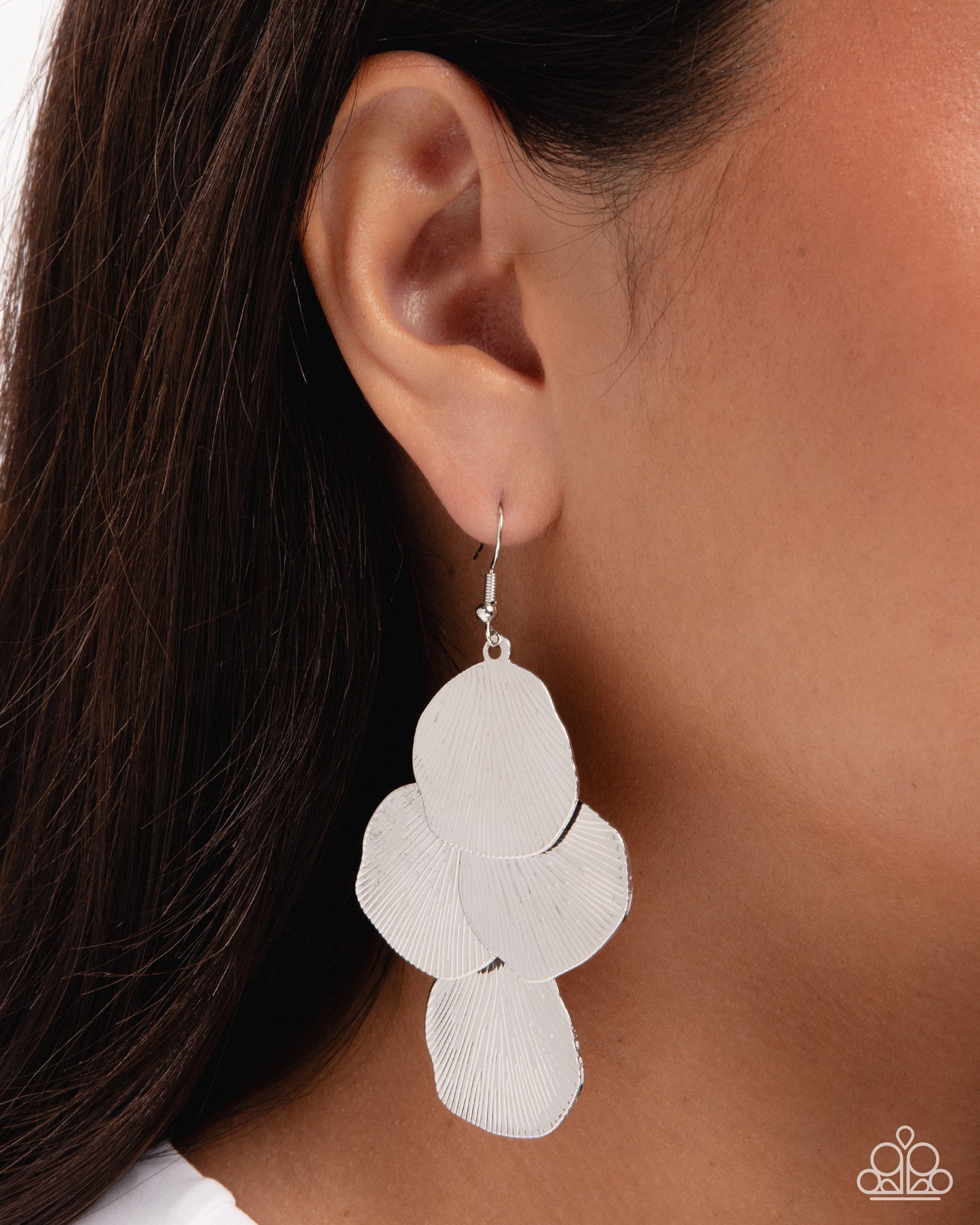 A close-up of a person's ear wearing a silver dangle earring with overlapping petal-like circular cutouts, against dark hair and skin.