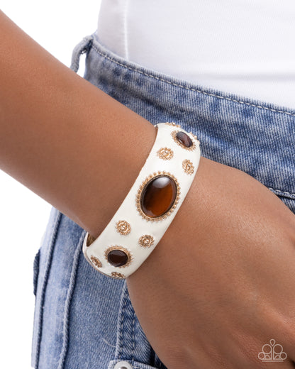 White leather bracelet with brown stones on a wrist against a denim background