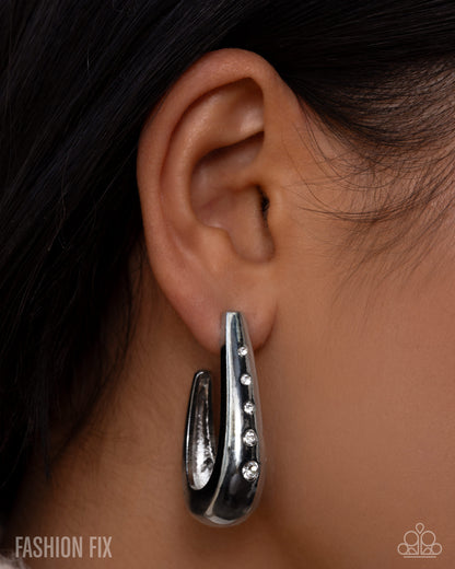 Silver hoop earring worn by a person with dark hair.