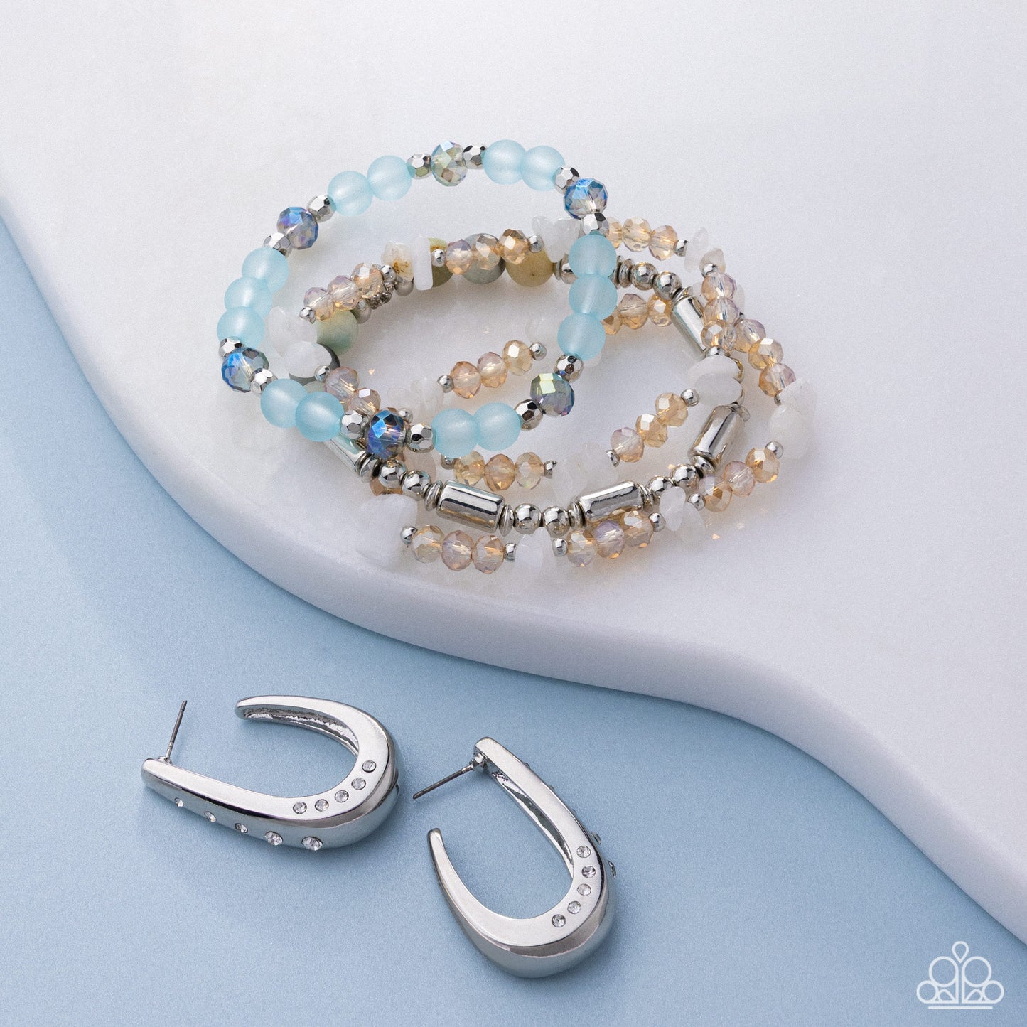 Beaded bracelet and silver hoop earrings on a light blue background